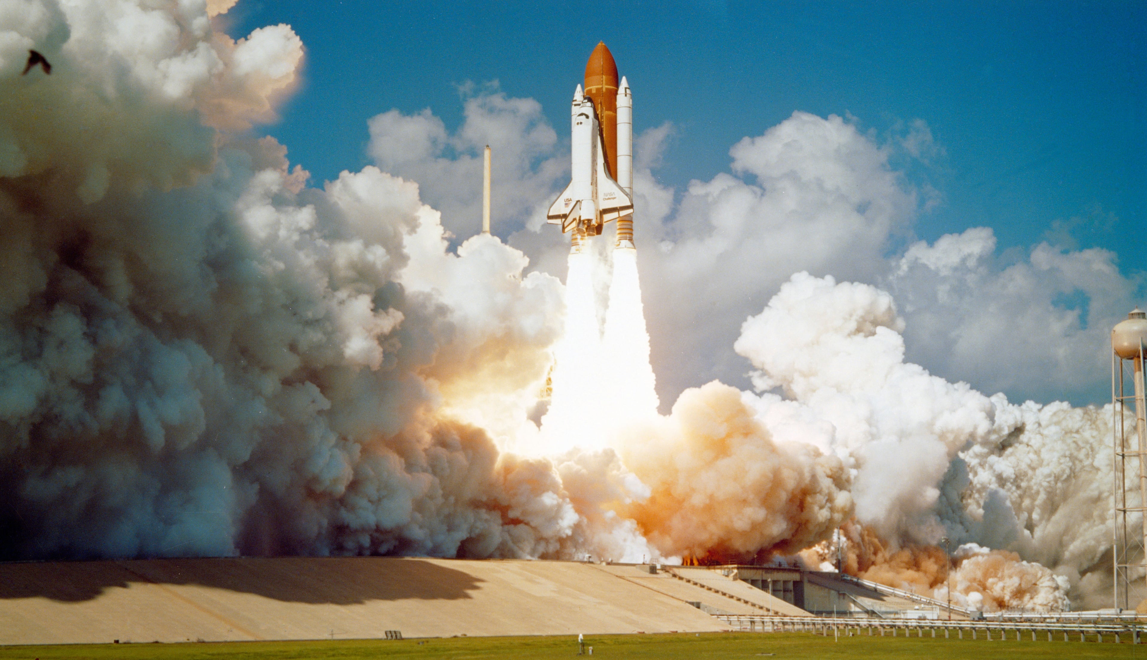 Space Shuttle Challenger lifting off from the launch pad on a clear day
